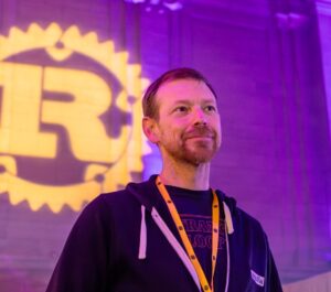 Jon Bauman standing in front of Rust logo projected on stone wall.